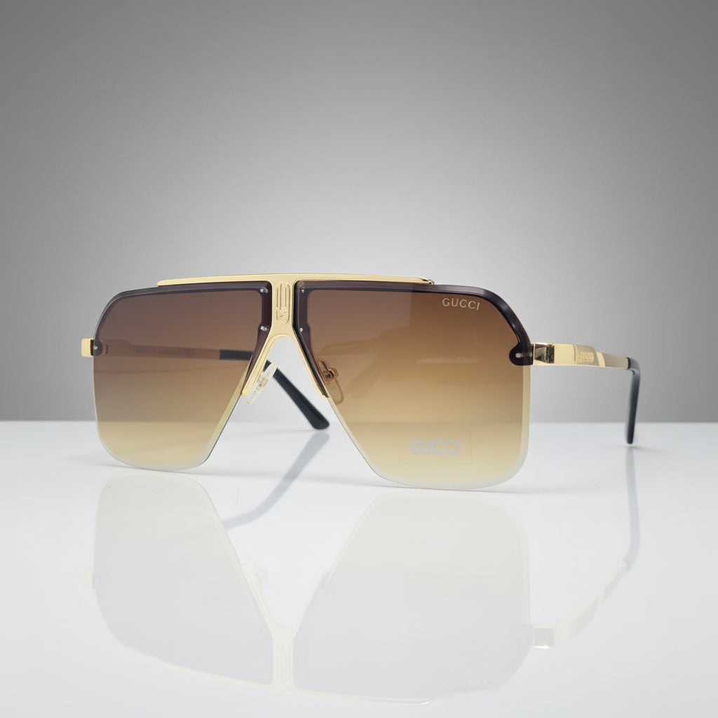 Aviator-style sunglasses with a gold-tone metal frame and gradient brown lenses, displayed on a reflective white surface against a white background.