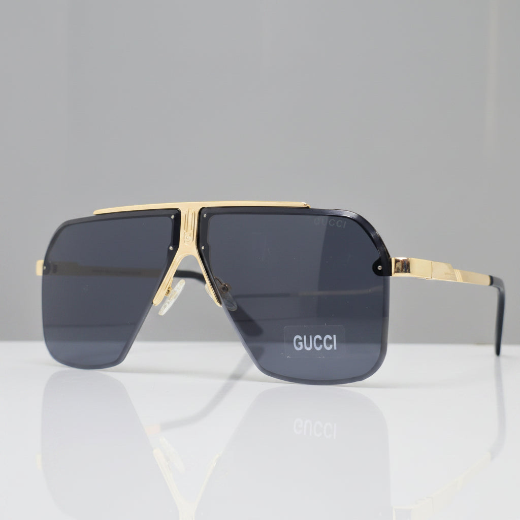 Gucci oversized square sunglasses with dark gray lenses and gold metal frames, displayed on a reflective white surface.