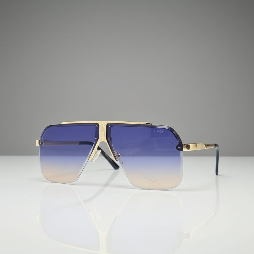 Aviator-style sunglasses with a gold-tone metal frame and gradient lenses that fade from blue at the top to clear at the bottom, displayed on a reflective white surface.