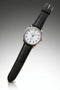 A wristwatch with a black textured leather strap, a silver-tone case, and a white dial with black Arabic numerals. The brand name 'Crown Royal' is visible on the dial.